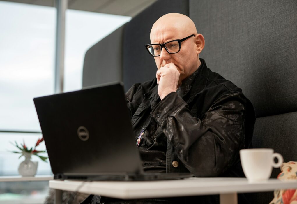a bald man sitting in front of a laptop computer